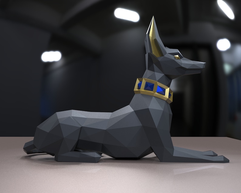 K&ouml;nnte beinhalten: Eine schwarze Anubis-Statue aus Origami mit goldenen Ohren und einem blauen Schmuckhalsband. Die Statue liegt auf einer hellgrauen Oberfl&auml;che.