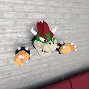 Op de afbeelding: Een papieren model van Bowser, een personage uit de Super Mario Bros. videogame-serie. Bowser is een grote, groene, vuurspuwende schildpad met rode stekels op zijn kop en schild. Hij wordt afgebeeld met zijn armen uitgestrekt, alsof hij aanvalt.