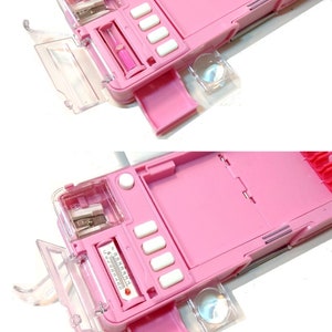 May include: Pink pencil case with a built-in sharpener, ruler, and magnifying glass. The case has a clear plastic lid and a compartment for pencils.