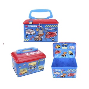 May include: Blue and red metal TOMICA toy box with a blue handle. The box features illustrations of various vehicles, including an ambulance, fire truck, and construction vehicles. The text "Let's Build TOMICA WORLD!" is also visible.