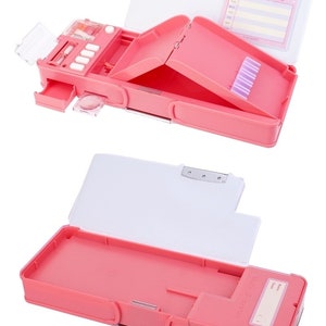 May include: Pink plastic pencil case with a built-in sharpener and a secret compartment. The case has a Hello Kitty design and a name tag.