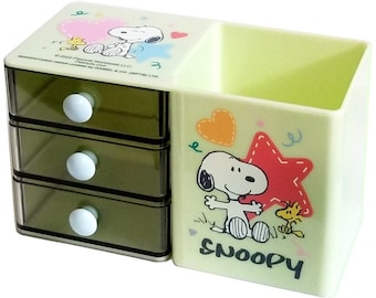 May include: A yellow plastic desk organizer with a drawer section and a pencil holder. The organizer features a cartoon image of Snoopy and Woodstock with the word "Snoopy" printed on the front.