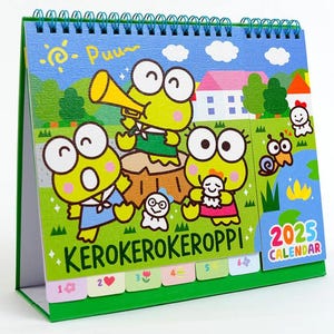 May include: A green desktop calendar featuring Kero Kero Keroppi characters. The calendar has a green cover with a spiral binding and a colorful design featuring Kero Kero Keroppi characters playing musical instruments. The calendar has a 2025 calendar tab on the right side.
