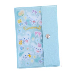 May include: A light blue zippered pouch with a flap closure and a snap button. The pouch features a clear plastic front with a repeating pattern of a white rabbit character with pink bows and the text "Cinnamoroll".