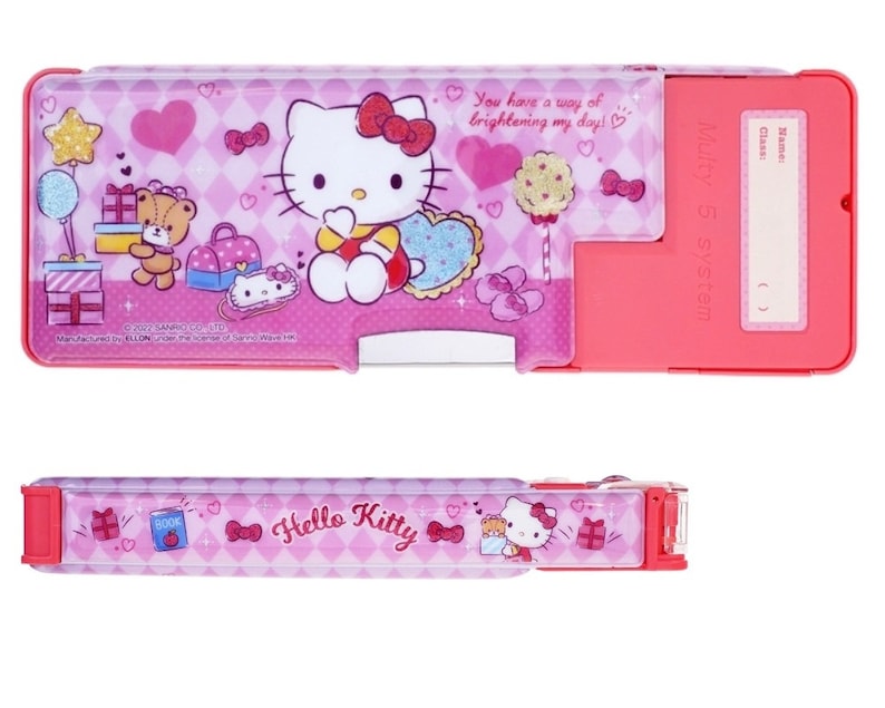 May include: Pink Hello Kitty pencil case with a clear plastic front and a pink and white checkered pattern. The case has a sliding compartment and a built-in pencil sharpener. The case features a Hello Kitty design with a pink bow and a heart. The text "You have a way of brightening my day!" is printed on the case. The text "Multy 5 system" is printed on the side of the case.