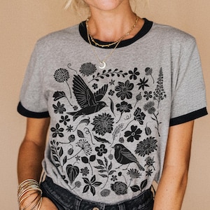 May include: Heather grey t-shirt with black trim featuring a black floral and bird design. The shirt has a crew neck and short sleeves. The text "heather grey/black" is visible in the bottom right corner.