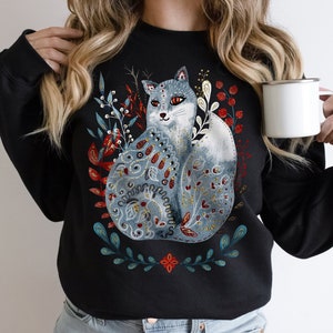 May include: Black sweatshirt with a blue and white fox illustration surrounded by floral designs in red, green, and gold.