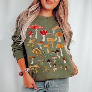 May include: A green sweatshirt with a colorful mushroom print. The mushrooms are in various shapes and sizes, with some having red caps and others having brown caps.