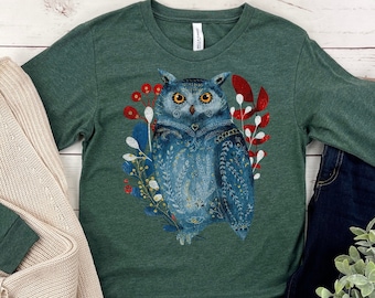 Pode incluir: Uma camiseta verde de manga comprida com um gráfico de coruja azul. A coruja está cercada por flores vermelhas e brancas. A camiseta é feita de um material macio e confortável.