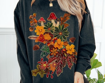 May include: A black sweatshirt with a colorful embroidered design of mushrooms, flowers, and leaves. The design is on the left side of the shirt.