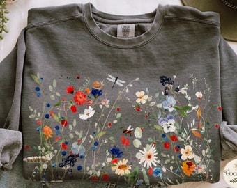May include: Gray sweatshirt with a floral print featuring a variety of flowers, leaves, berries, a dragonfly, a snail, and a bee. The print is in shades of red, blue, yellow, green, and white.
