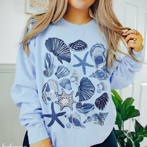 May include: A light blue sweatshirt with a graphic print of various seashells and starfish in shades of blue and white.