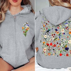 May include: A grey zip-up hoodie with a floral print on the back and a smaller floral print on the front. The hoodie has a hood and a zipper closure. The text "sport grey" is visible at the bottom of the image.