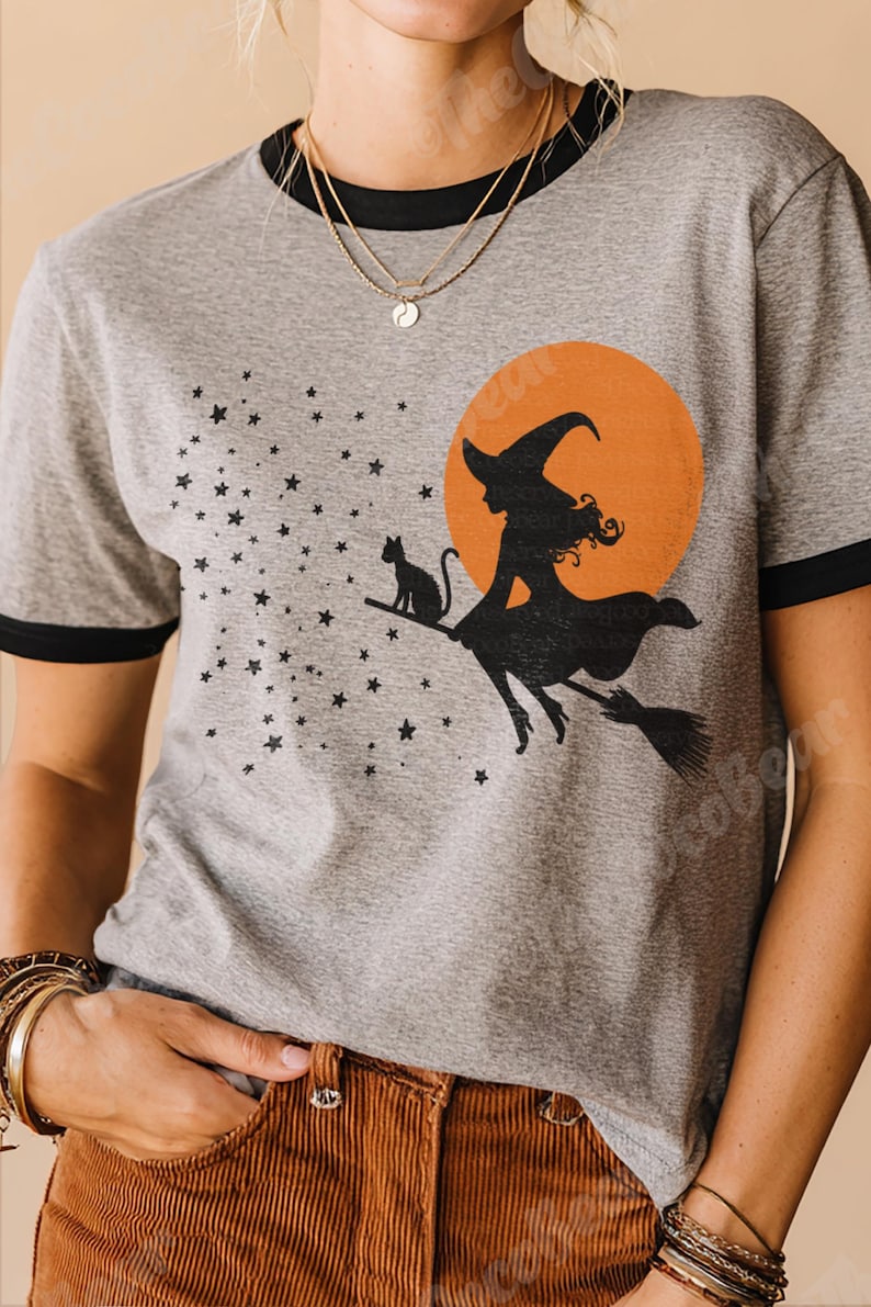 May include: Grey ringer t-shirt featuring a black witch silhouette riding a broom in front of an orange moon. A black cat sits on the broom. Stars are scattered across the shirt. The tee has black trim around the collar and sleeves.