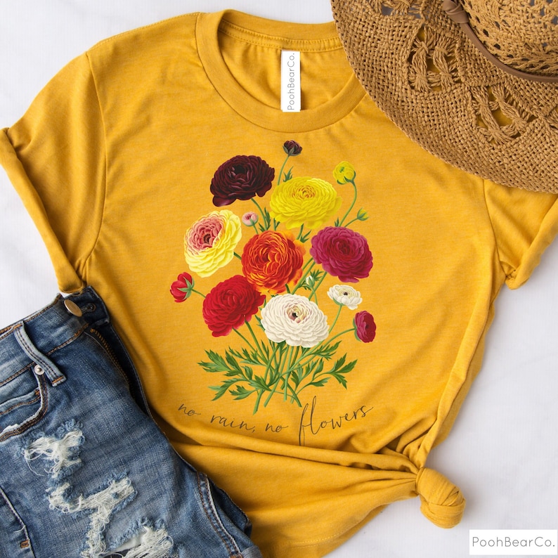 May include: A mustard yellow t-shirt with a floral print of red, yellow, white, and purple flowers. The text "no rain, no flowers" is printed below the flowers.