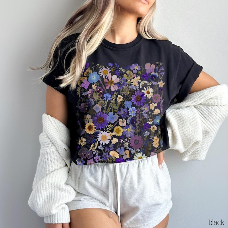 May include: A black cropped t-shirt with a floral print featuring a variety of purple, blue, and yellow flowers. The shirt has a relaxed fit and a crew neckline.