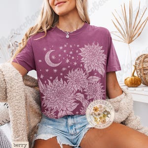 Pode incluir: Camiseta cor de berry com um design floral e celestial. O gr&aacute;fico inclui uma lua crescente, estrelas e flores grandes. A camisa tem gola redonda e caimento solto. Design original CocoBear.