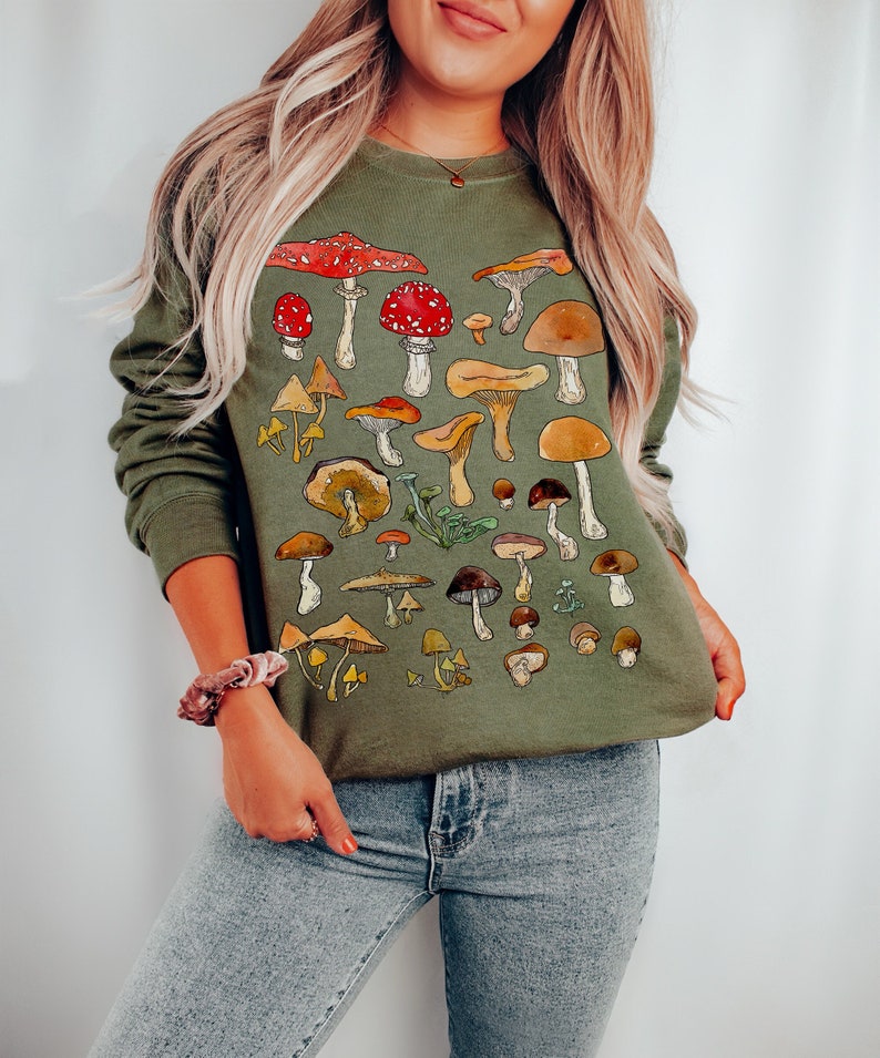 May include: A green sweatshirt with a colorful mushroom print. The mushrooms are in various shapes and sizes, with some having red caps and others having brown caps.