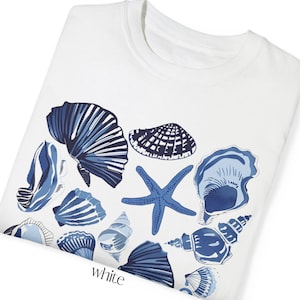 Puede incluir: Camiseta blanca con un dise&ntilde;o de conchas marinas azul y blanco. El dise&ntilde;o incluye varias conchas, una estrella de mar y algunas conchas m&aacute;s peque&ntilde;as.