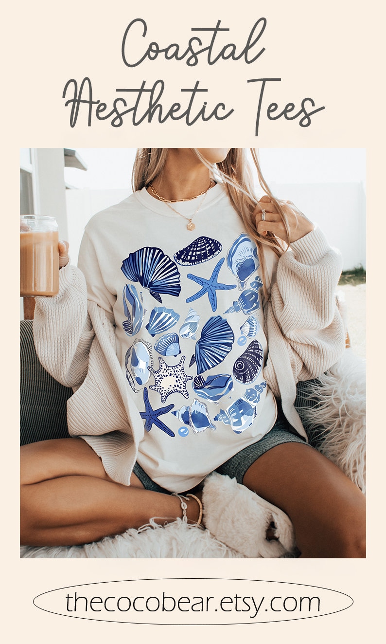 Puede incluir: Una sudadera blanca con un dise&ntilde;o de conchas marinas y estrellas de mar azules y blancas. El texto "thecocobear.etsy.com" est&aacute; impreso en la parte inferior de la imagen.