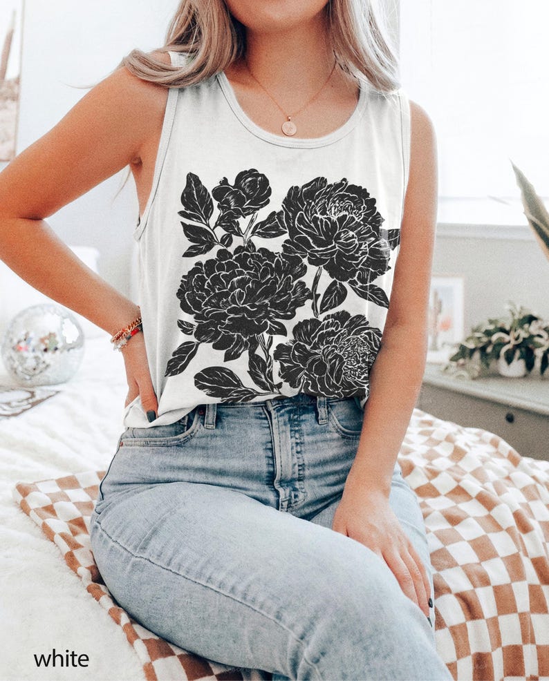 May include: A white sleeveless tank top featuring a large black graphic print of blooming peonies with detailed petals and leaves. The garment has a round neckline and is paired with light blue denim jeans. The design is centered on the front.
