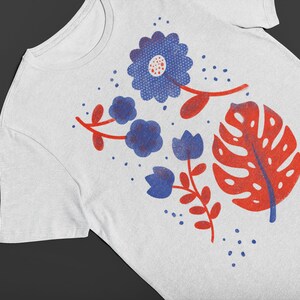Puede incluir: Camiseta blanca con un dise&ntilde;o floral azul y rojo. El dise&ntilde;o incluye una flor azul grande con un centro rojo, flores azules m&aacute;s peque&ntilde;as y una hoja roja.