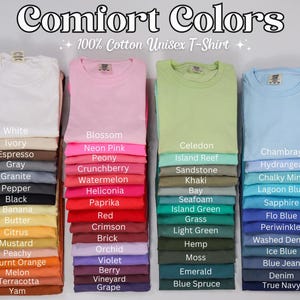 Pode incluir: Pilhas de camisetas unissex Comfort Colors 100% algod&atilde;o dobradas em v&aacute;rias cores, incluindo branco, rosa, verde e azul. Cada pilha exibe um nome de cor diferente, como "Blossom", "Celedon" e "Chambray".