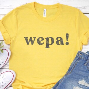 May include: Yellow t-shirt with the word "wepa!" printed in black.