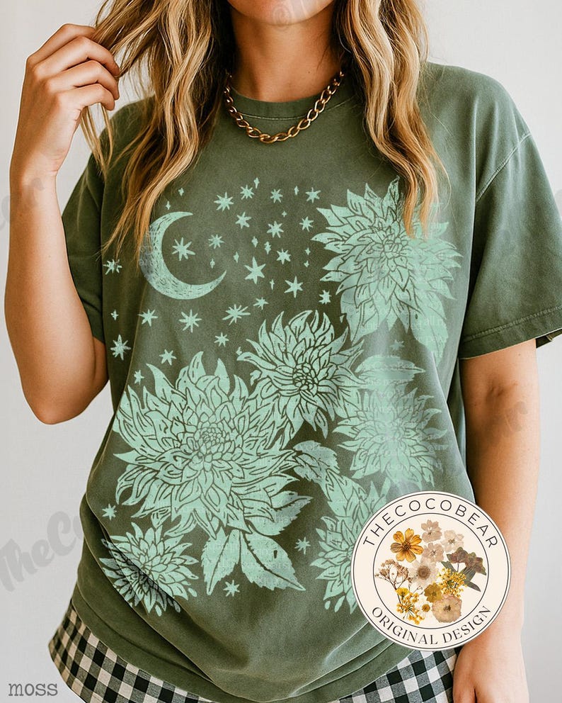 May include: Moss green t-shirt featuring a floral and celestial design. The design includes a crescent moon, stars, and large flowers in a lighter green hue. The shirt has a relaxed fit and short sleeves. The Coco Bear original design logo is visible.