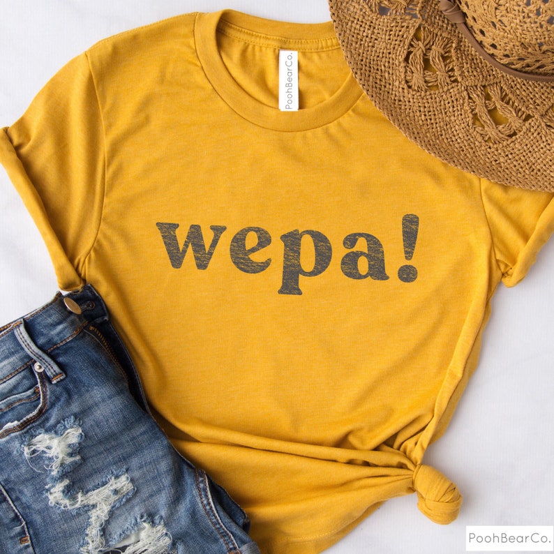 May include: A mustard yellow t-shirt with the word "wepa!" printed in black on the front. The shirt is made of a soft, comfortable material and has a relaxed fit.