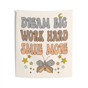 May include: A beige tapestry with the text "Dream Big Work Hard Smile More" in a retro font. The tapestry features a butterfly with orange, yellow, and gray wings and a crescent moon.