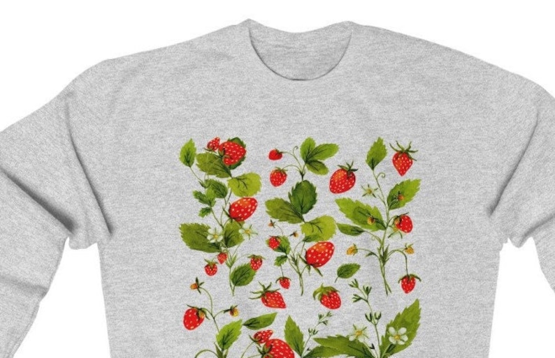 Puede incluir: Una sudadera gris claro con un dise&ntilde;o bot&aacute;nico de fresas. El dise&ntilde;o incluye fresas rojas, hojas verdes y peque&ntilde;as flores blancas. Las fresas est&aacute;n en varias etapas de madurez.