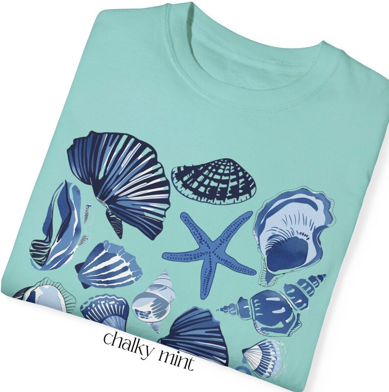 Puede incluir: Una camiseta azul turquesa con un dise&ntilde;o de varias conchas marinas azules y blancas y una estrella de mar. El texto "chalky mint" est&aacute; impreso en la parte inferior de la camiseta.