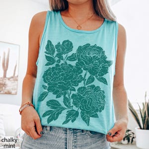 May include: A chalky mint sleeveless tank top featuring a large, dark green graphic print of three blooming peony flowers with detailed leaves and stems. The garment has a round neckline and is worn with a gold chain necklace.