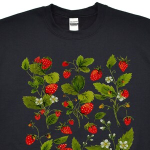 Puede incluir: Sudadera negra con un dise&ntilde;o bot&aacute;nico de fresas. El dise&ntilde;o incluye fresas rojas, hojas verdes y peque&ntilde;as flores blancas. Las fresas est&aacute;n dispersas por la parte delantera de la sudadera.