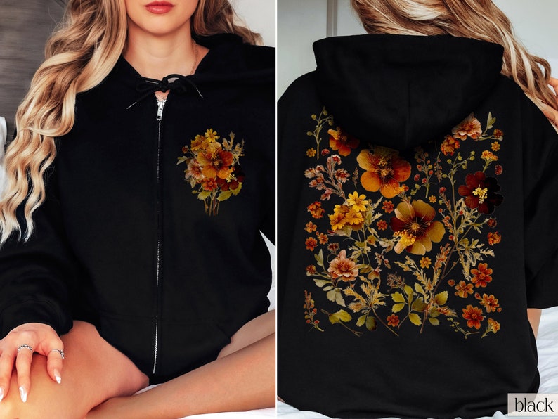 May include: Black zip-up hoodie with a floral print featuring dried flowers in shades of orange, yellow, and brown. The print is on the front and back of the hoodie.