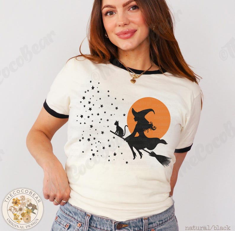 May include: Cream ringer t-shirt with black trim, featuring a Halloween design. The graphic shows a witch on a broom with a cat, stars, and an orange moon. The text "natural/black" is at the bottom right.