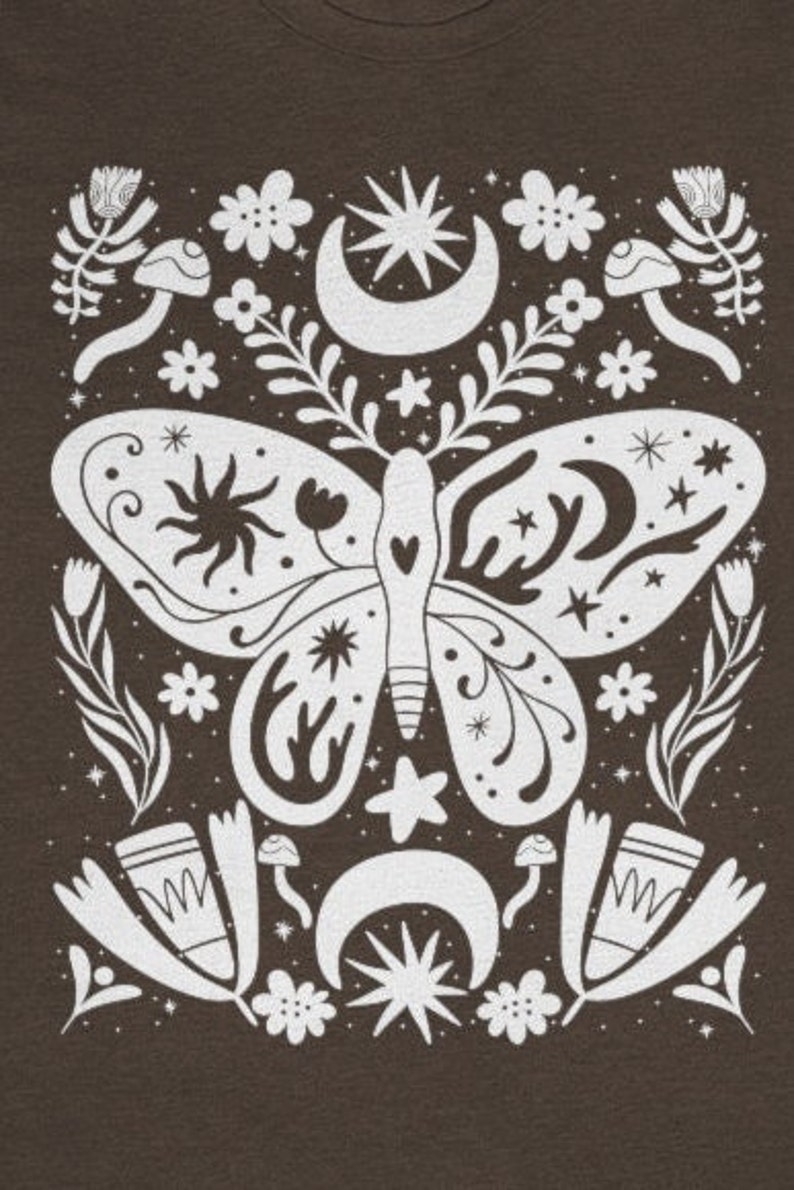 Puede incluir: Un dise&ntilde;o gr&aacute;fico blanco sobre un fondo marr&oacute;n presenta una mariposa estilizada con elementos florales y celestiales. La mariposa tiene un cuerpo en forma de coraz&oacute;n y alas intrincadas con estrellas, lunas y soles. El dise&ntilde;o est&aacute; rodeado de flores, hongos y lunas crecientes.