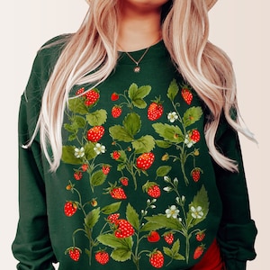 Puede incluir: Una sudadera verde oscuro con un dise&ntilde;o de acuarela de fresas, hojas y flores blancas. Las fresas son rojas y las hojas son verdes. La sudadera tiene mangas largas y cuello redondo.
