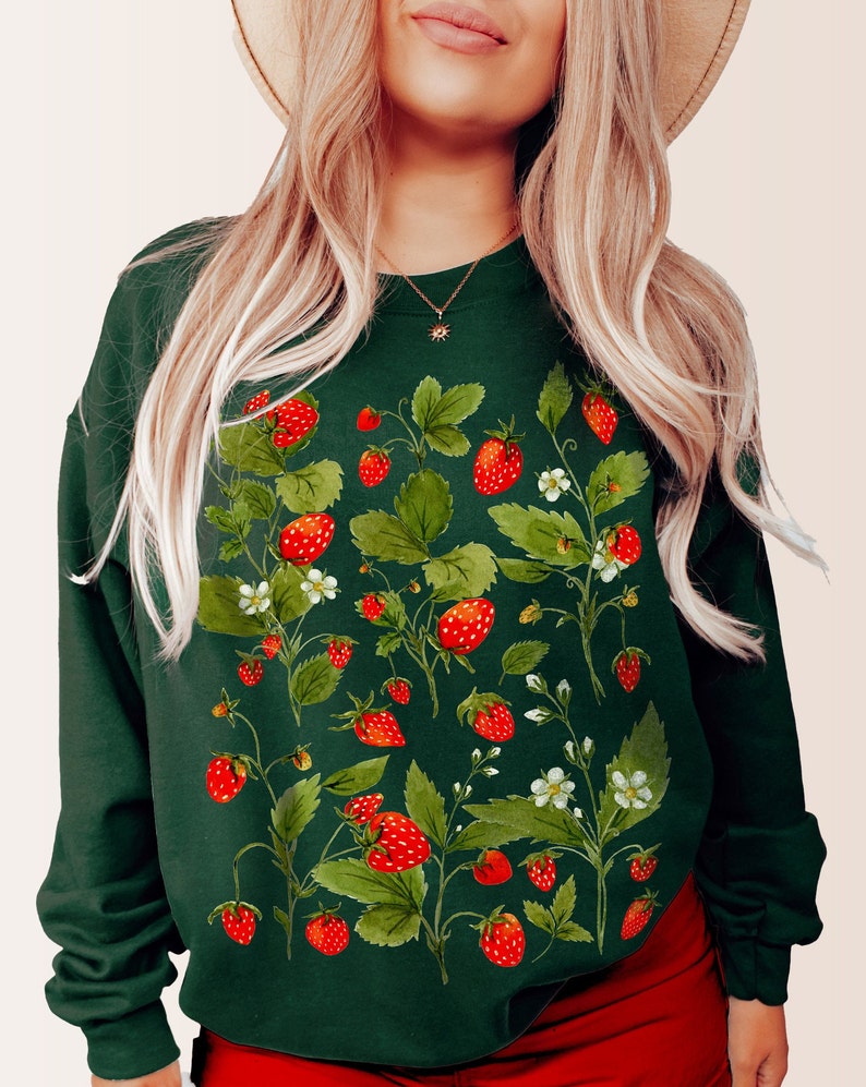 Puede incluir: Una sudadera verde oscuro con un dise&ntilde;o de acuarela de fresas, hojas y flores blancas. Las fresas son rojas y las hojas son verdes. La sudadera tiene mangas largas y cuello redondo.