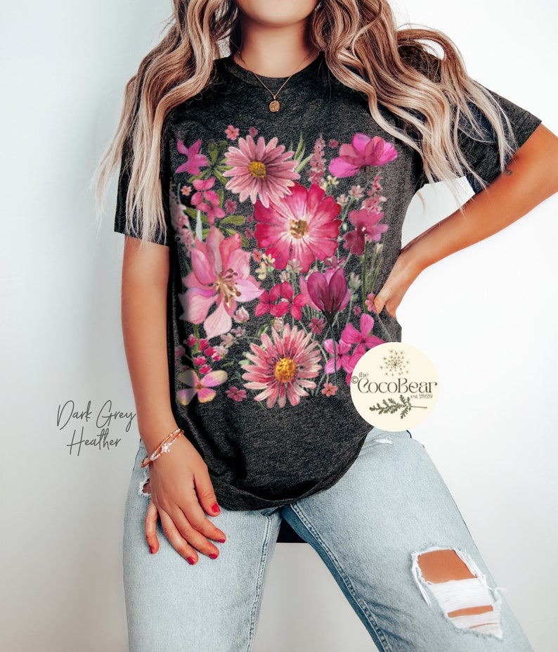May include: Dark grey heather t-shirt with a colourful floral print in pink and magenta hues. The design showcases a variety of flowers and leaves. The text "The CocoBear" is visible on the right side of the shirt.