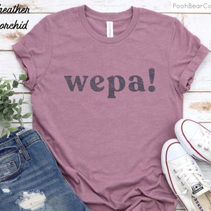 May include: A heather orchid t-shirt with the word "wepa!" printed in black on the front. The shirt is shown on a model wearing blue jeans and white sneakers.
