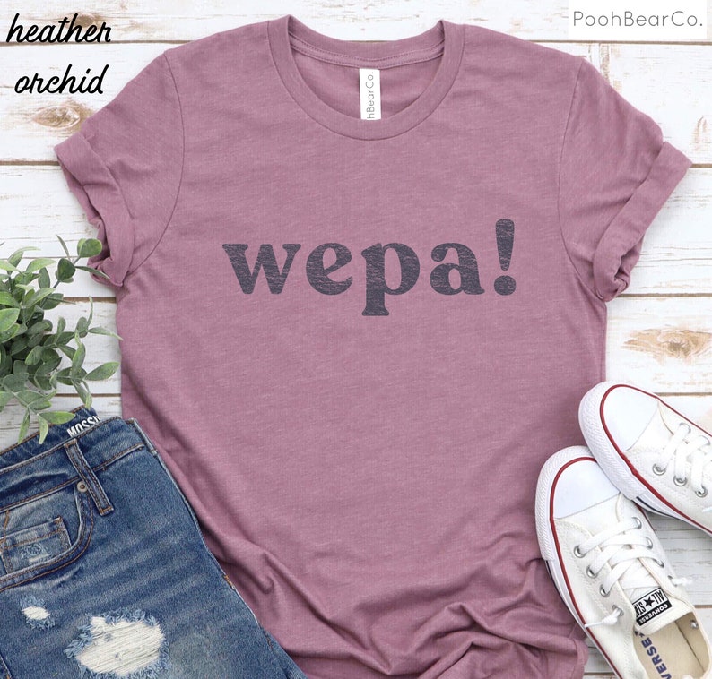 May include: A heather orchid t-shirt with the word "wepa!" printed in black on the front. The shirt is shown on a model wearing blue jeans and white sneakers.