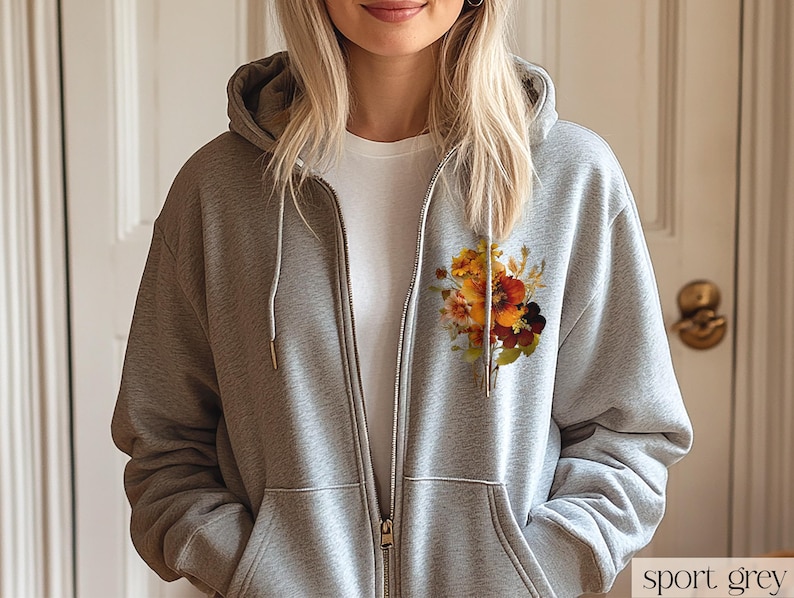 May include: A gray zip-up hoodie with a floral print on the left side of the chest. The print features a bouquet of orange, yellow, and brown flowers.
