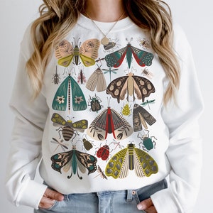 May include: White sweatshirt with a colorful print of various insects, including butterflies, moths, and beetles. The print is a stylized design with a vintage aesthetic.