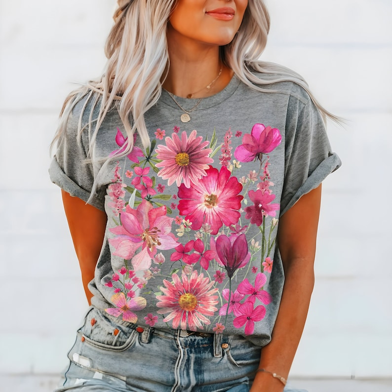 May include: Grey t-shirt with a colourful floral print. The design features a collection of pink and magenta flowers, including daisies and tulips. The short-sleeved tee is made of a soft material.