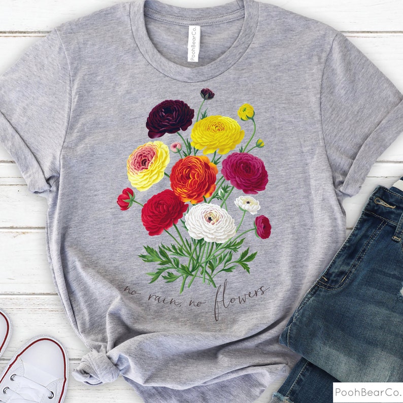 May include: Gray t-shirt with a floral design featuring a bouquet of colorful ranunculus flowers. The text "no rain, no flowers" is printed below the flowers.