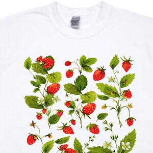 Puede incluir: Sudadera blanca con un dise&ntilde;o de acuarela de fresas, hojas verdes y flores blancas. Las fresas son rojas con peque&ntilde;as semillas amarillas. El dise&ntilde;o se extiende por la parte delantera de la sudadera.