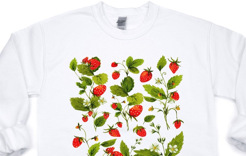 Puede incluir: Sudadera blanca con un dise&ntilde;o de acuarela de fresas, hojas verdes y flores blancas. Las fresas son rojas con peque&ntilde;as semillas amarillas. El dise&ntilde;o se extiende por la parte delantera de la sudadera.