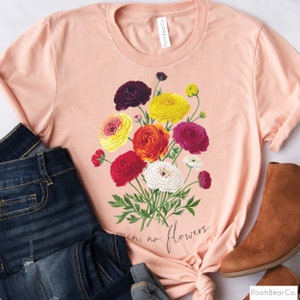 May include: A peach-colored t-shirt with a floral design featuring a bouquet of red, yellow, white, and purple flowers. The text "rain, no flowers" is printed on the shirt.